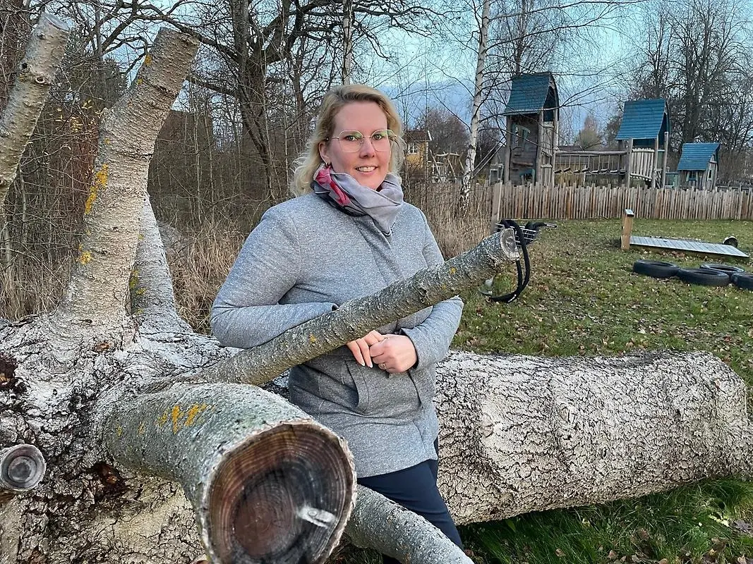 Sofie Lindberg, ordförande i Vittinge byalag, sitter på ett omkullfallet träd i parken i Vittinge. I bakgrunden ser man utegymmet och lekparken. Det ser riktigt höstigt ut.