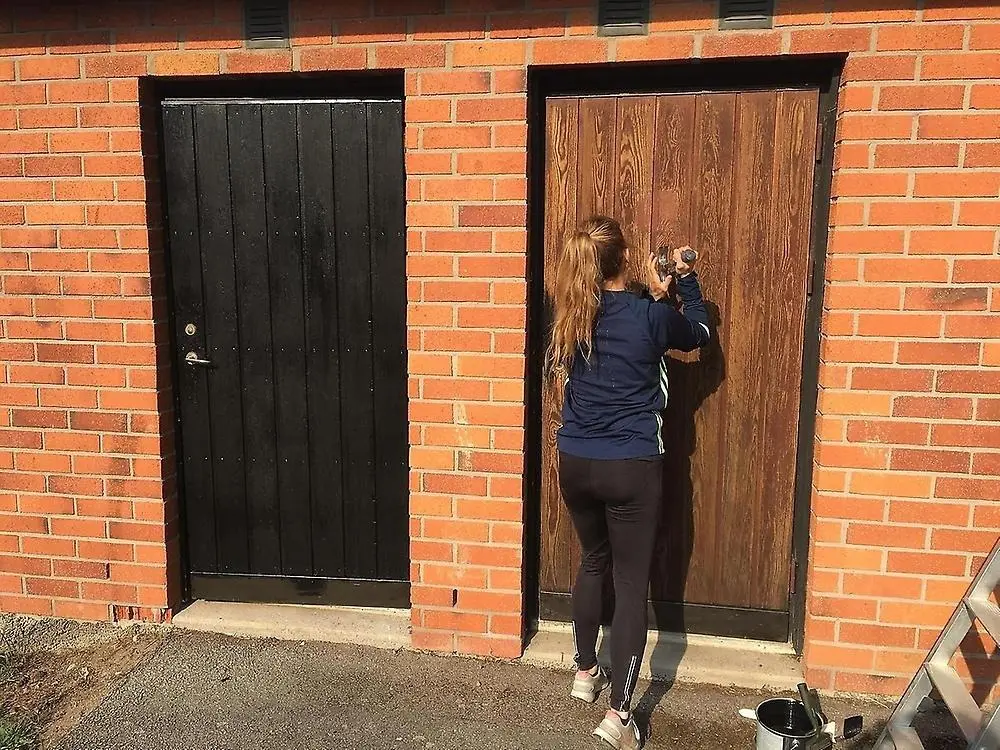 Ung tjej tar bort gammal färg från en dörr som ska målas