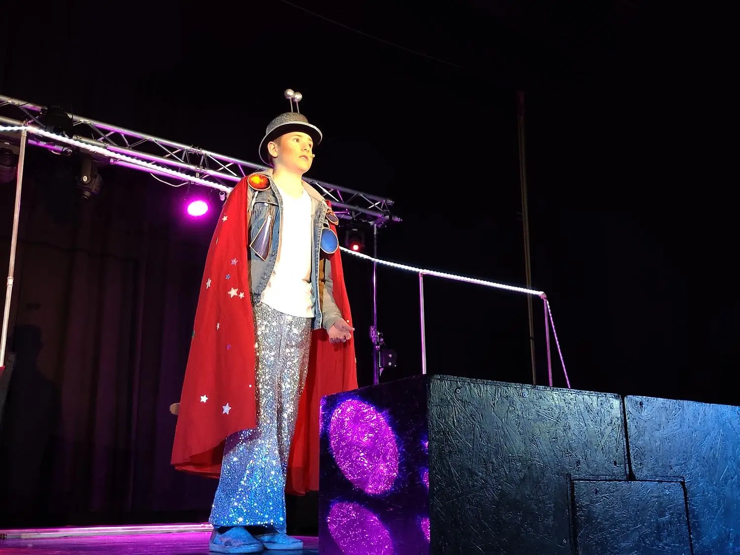 Pojke på scen med röd cape och glittrig hatt