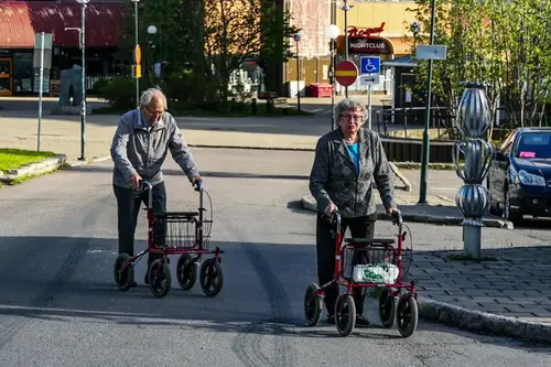 En äldre kvinna och man går på gatan med rollatorer