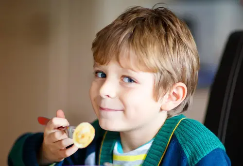 Liten pojke äter pasta inomhus vid ett bord