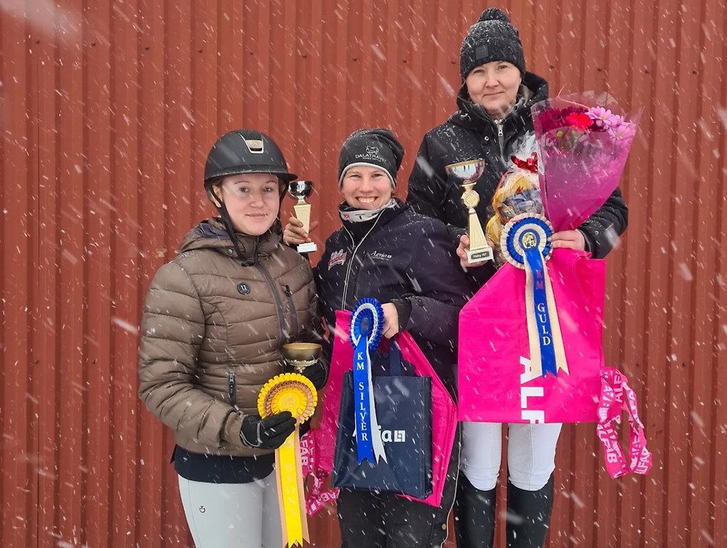 Tre glada vinnare i klassen egen häst i KM i dressyr på Heby Ryttarförening står ute i snöyra och tar emot sina priser.